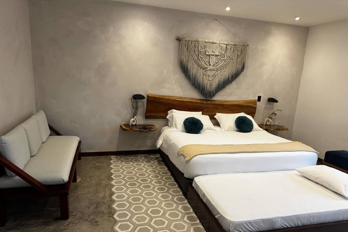 Une chambre à coucher moderne avec un grand lit, deux tables de chevet, un banc en bois et un sol orné d’un motif géométrique.