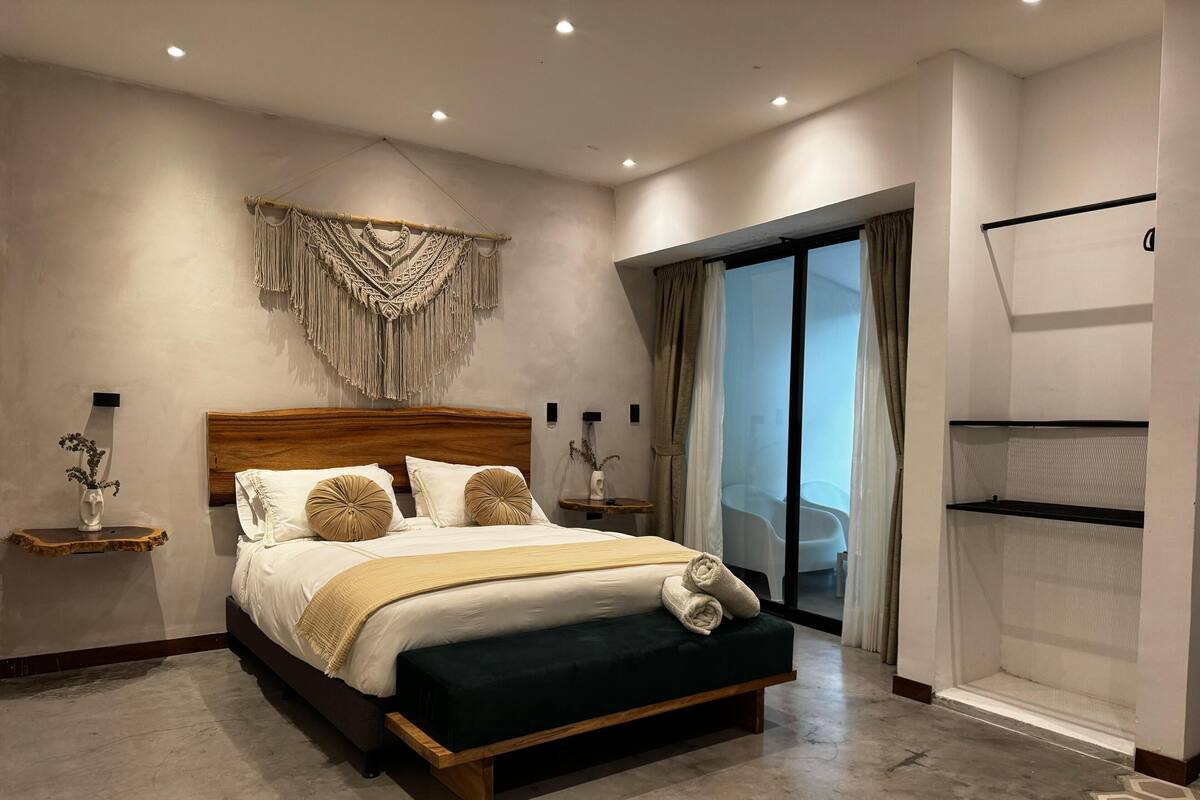 Une chambre moderne avec un grand lit, une tête de lit en bois et une décoration murale en macramé.