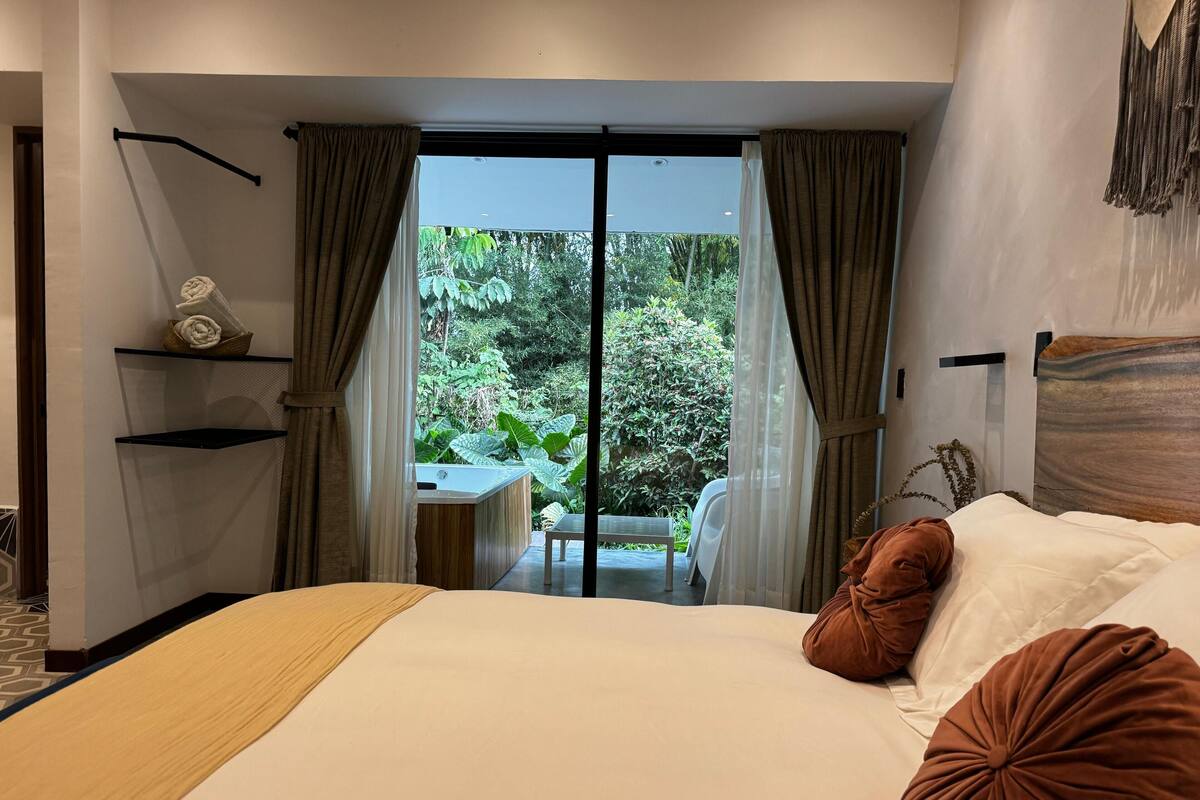 Une chambre avec un grand lit, une vue sur la verdure et une petite table avec des chaises.