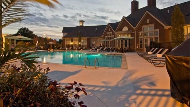 Un hotel con piscina, sillas de descanso y un patio cubierto.
