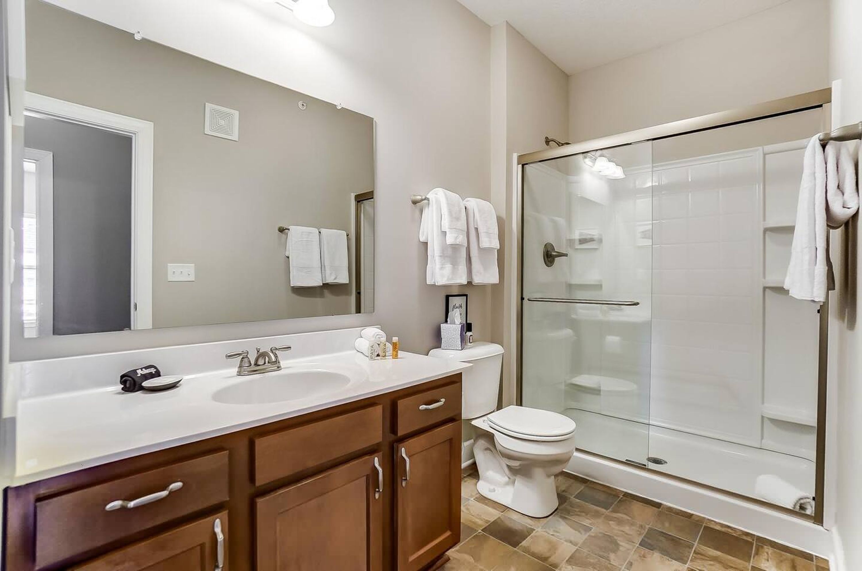 A modern bathroom with a large mirror, a sink, a toilet, and a glass-enclosed shower.