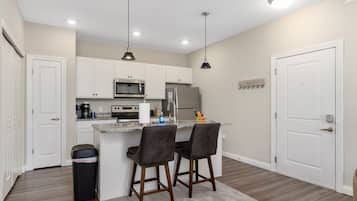 A modern kitchen with white cabinets, a stainless steel refrigerator, a microwave, and two bar stools.