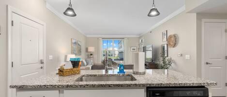 A modern kitchen with granite countertops, a stainless steel dishwasher, and pendant lighting.