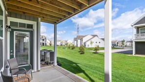 A covered porch with two wicker chairs and a small table, overlooking a well-maintained lawn and neighboring houses. - Powell Retreat Attached Garage Walk-in Shower (Powell)
