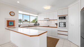 Une cuisine moderne avec des meubles blancs, un plan de travail en bois, un four encastré et une grande fenêtre donnant sur un paysage verdoyant.
