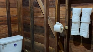A wooden bathroom with a toilet, a towel rack, and a wooden door. - Green Jay Cabin 2 (Cristo Rey)