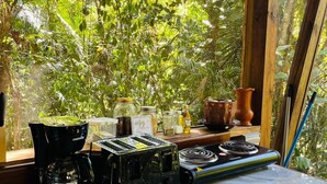 A kitchen with a coffee maker, toaster, and a stove. There are jars and a bottle on the counter. - Green Jay Cabin 2 (Cristo Rey)