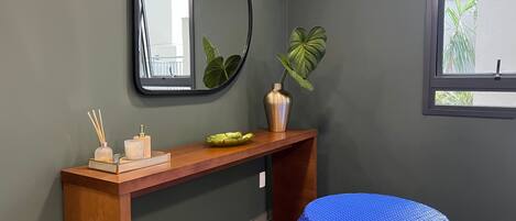 Un baño con tocador de madera, espejo, planta en maceta y un taburete tejido azul.
