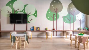 Une salle de jeux pour enfants avec une grande fresque murale, un téléviseur à écran plat et une variété de jouets rangés sur des étagères.