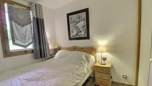 Un dormitorio con una cama individual, una mesita de noche con lámpara, un cuadro enmarcado en la pared y una ventana con cortinas.