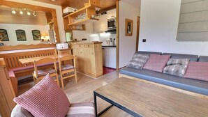 Un espacio de sala cómodo con sofá, una mesa de comedor y sillas. Hay una cocina con microondas y refrigerador.
