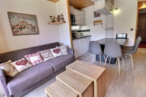 A cozy living area with a sofa, a wooden coffee table, and a dining table with chairs. A kitchen is visible in the background. - 10m from ski slopes, 3rd floor, view mountain, balcony, 25m², Méribel-Mottaret (Méribel - Les Allues)