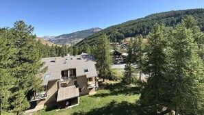 Un edificio de dos pisos con techo inclinado, rodeado de árboles y montañas.