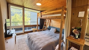 Un dormitorio de cabaña de madera con una cama litera, un escritorio con una computadora portátil y una ventana con vistas a un bosque.