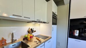Una cocina moderna con armarios blancos, un lavamanos de acero inoxidable, una encimera con frutas y utensilios, y un horno empotrado.