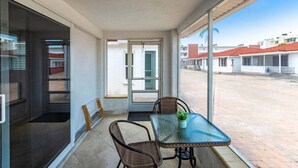 Un balcón con una mesa de vidrio y sillas de mimbre, con vistas a una zona residencial.