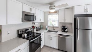 A modern kitchen with white cabinets, stainless steel appliances, and a ceiling fan.