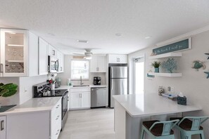 A modern kitchen with white cabinetry, stainless steel appliances, and a central island with bar stools.