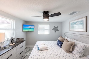 A bedroom with a bed, a ceiling fan, a TV, a starfish decoration, and a framed picture on the wall.
