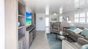 Ein geräumiges Wohnzimmer mit Fernseher, Sitzgelegenheit und Blick ins Freie.