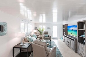 A living room with a sofa, armchairs, a coffee table, a TV, and a bookshelf. - Casa Blanca - Villa A01 (Sarasota)