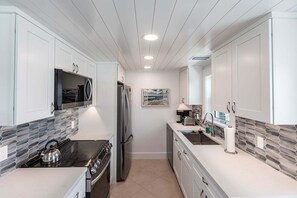 A modern kitchen with white cabinetry, a stainless steel refrigerator, a stove, and a microwave.