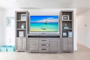 Una sala de estar con un televisor montado en un mueble bajo de madera, un cuadro en la pared y un estante con objetos decorativos.