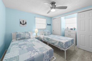 A bedroom with two beds, a ceiling fan, and a window with blinds.