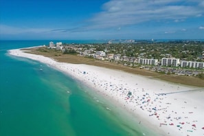 An aerial view of a coastal area with a wide beach, buildings, and a clear sky.
