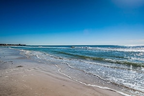 A beach with waves, a clear sky, and a distant shoreline.