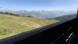 Vista da janela com um monte arborizado e uma cordilheira ao longe.
