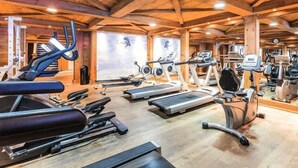 Uma academia com diversos equipamentos de cardio, vigas de madeira no teto e um amplo painel de espelhos.