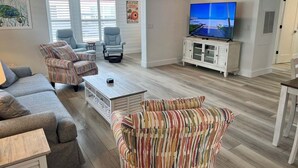 Ein Wohnzimmer mit Sofa, Sesseln, Couchtisch, Fernseher und Schrank.