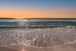 A beach with waves, a clear sky, and a sunset.