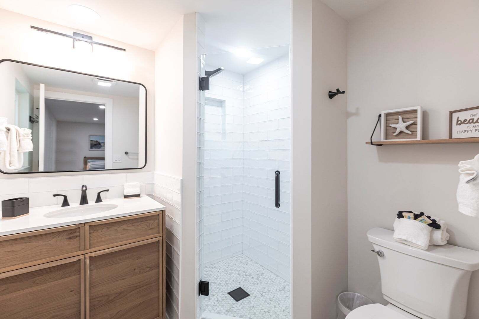 Un baño moderno con ducha acristalada, inodoro blanco y tocador con espejo y lavabo.
