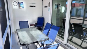 A small room with a glass door leading to an outdoor area, a table with chairs, and a clock on the wall. - Csa Blanca - Villa B18 (Sarasota)