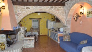 A rustic kitchen with a stone archway, a blue sofa, and a dining area with a table and chairs. - Agriturismo Bellavista between Amiata and Val dórcia - Mountain apartment (Toscana)