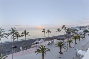 Eine Uferpromenade mit Palmen, einem Strand und Gebäuden im Hintergrund.