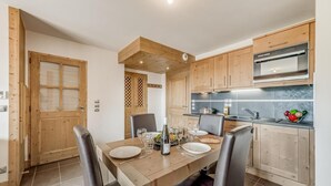 Eine moderne Küche mit Holzschränken, einem eingebauten Backofen und einem Essbereich mit Tisch für vier Personen.
