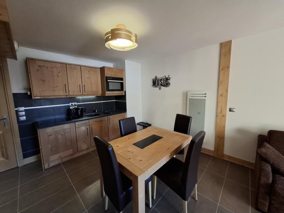 A compact kitchen with wooden cabinets, a central island, and a dining table with chairs.
