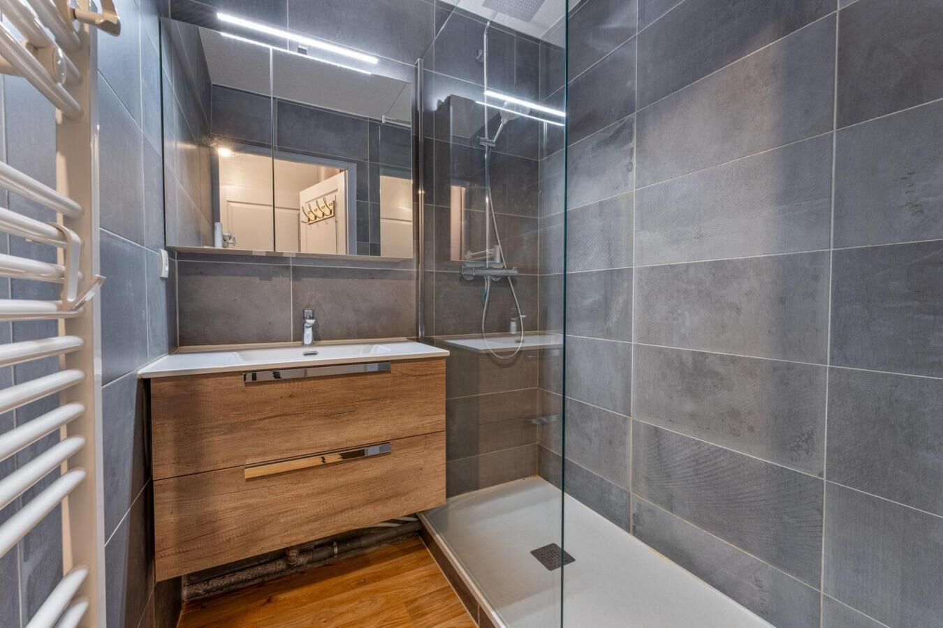 Un bagno moderno con un mobile bagno in legno, box doccia in vetro e piastrelle grigio scuro.