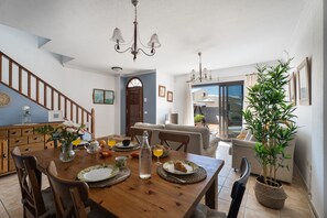 A dining area with a wooden table, chairs, a chandelier, and a potted plant.
