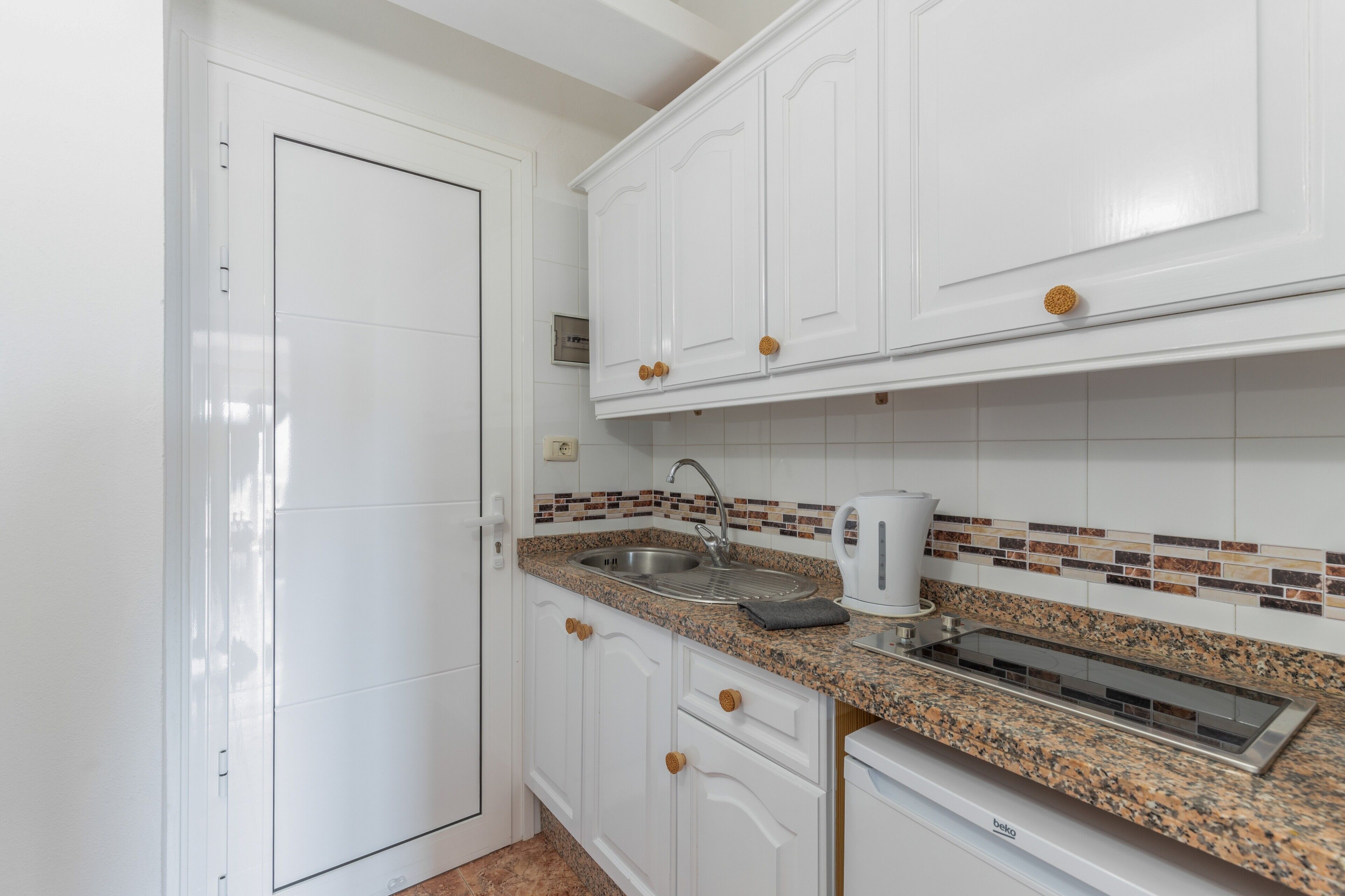 A kitchen with white cabinets, a granite countertop, a stainless steel sink, and a built-in range hood.