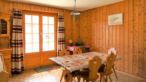 Una habitación con paneles de madera, una mesa de comedor, sillas, un radio y una puerta con cortinas.