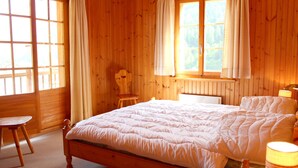 Una habitación de madera con una cama, una silla y un ventanal con cortinas.