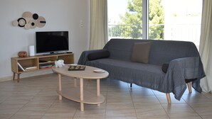 Een woonkamer met een grijze bank, een houten salontafel, een flatscreen televisie op een houten standaard en een decoratief kunstwerk aan de muur.