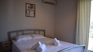 Een net opgemaakt bed met witte lakens en twee opgerolde handdoeken, een nachtkastje met een lamp, en een wandairconditioner.