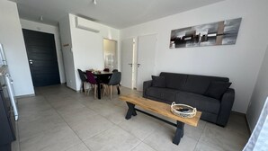 Un salon moderne avec un canapé gris, une table basse en bois et un coin repas comprenant une table et des chaises.