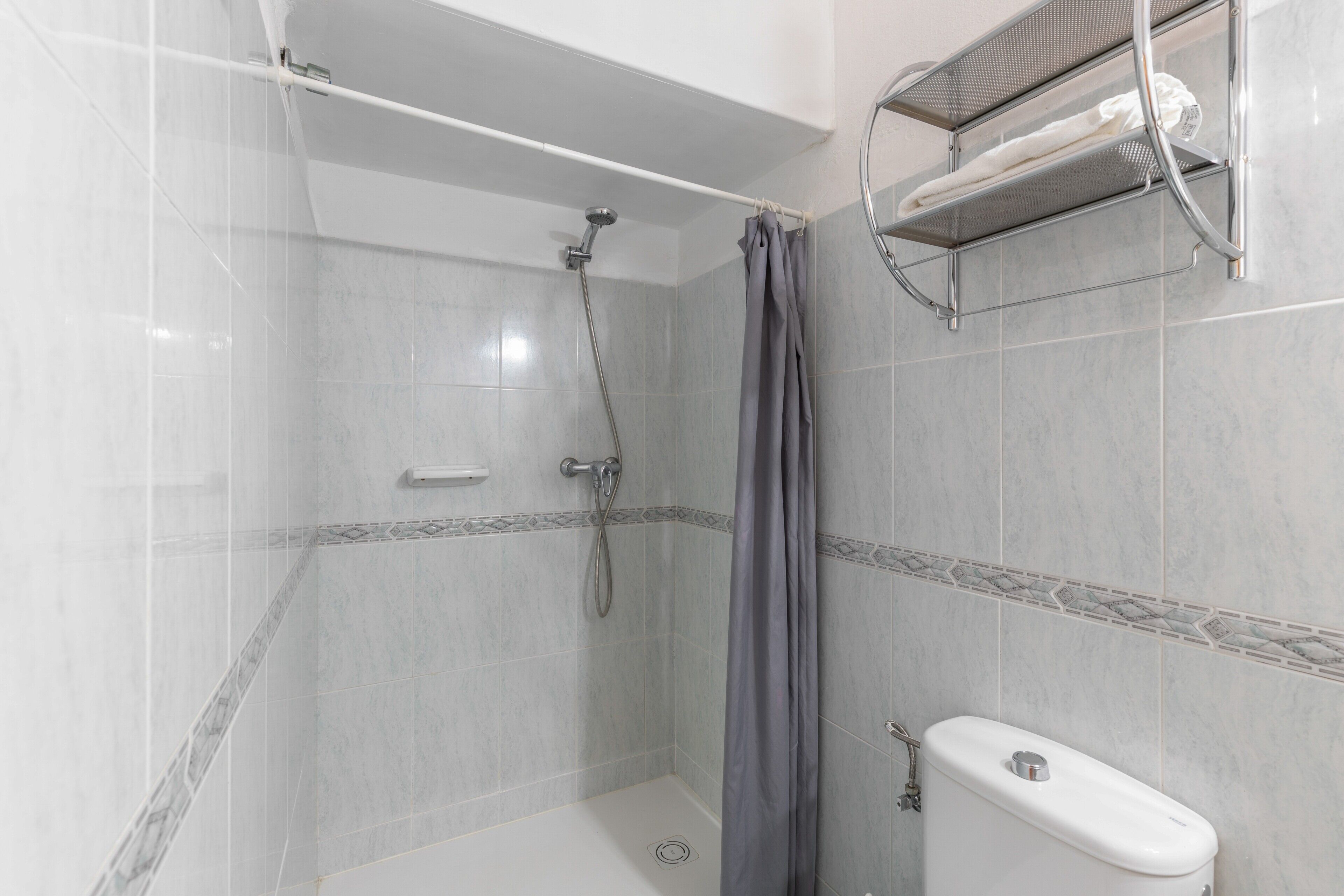 A shower with a showerhead, a curtain, and a towel rack with a towel.