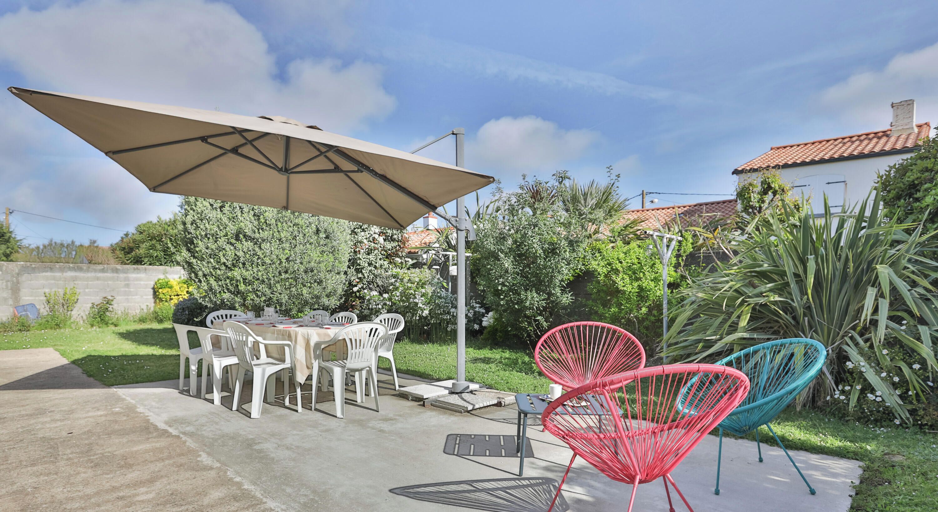An outdoor patio with a table and chairs, a large umbrella, and colorful chairs.